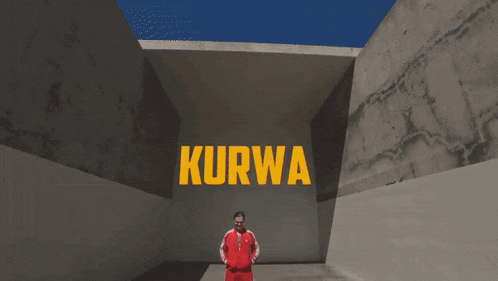 a man wearing a red adidas jacket stands in front of a wall with kurwa written on it