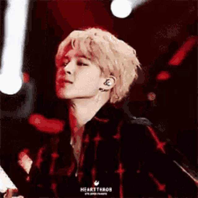 a young man with blonde hair is standing on a stage wearing a plaid shirt and headphones .