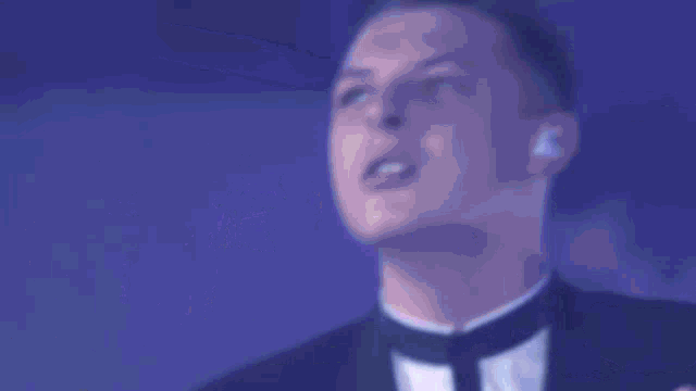 a man in a tuxedo sings into a microphone in front of a drum set that has the letter n on it