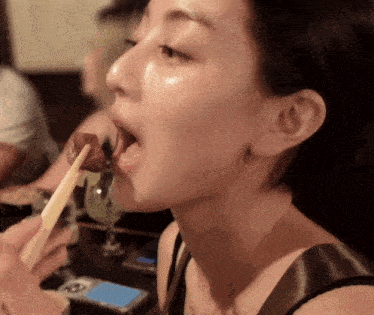 a woman is eating a piece of meat with chopsticks while looking at her phone