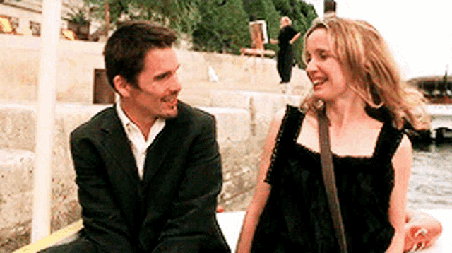 a man in a suit and a woman in a black dress are looking at each other and smiling