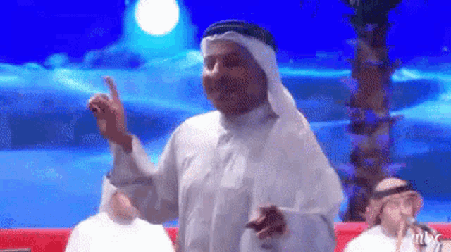 a man in a white robe is giving a thumbs up in front of a blue background