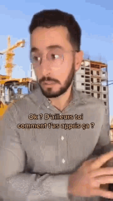 a man with glasses is standing in front of a construction site .