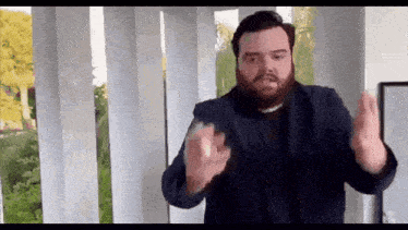 a man with a beard is standing in a room with columns and making a funny face .