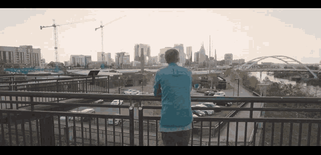 a man in a blue shirt is standing on a balcony overlooking a city