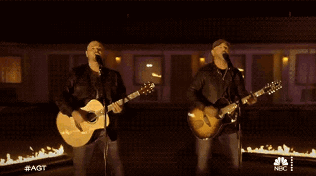 two men are singing and playing guitars in front of a motel