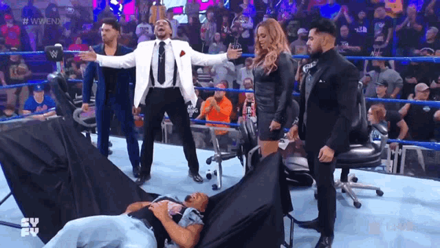 a man in a suit and tie is standing in a wrestling ring with his arms outstretched ..