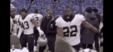 a group of football players are standing on the sidelines of a field .
