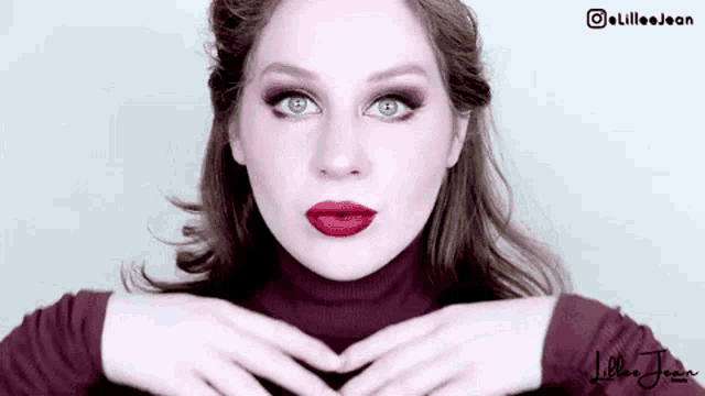 a woman wearing red lipstick and a turtleneck sweater is making a heart shape with her hands .