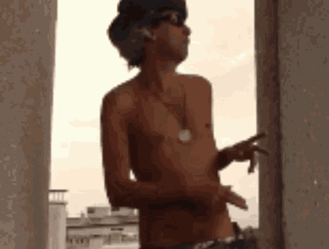 a shirtless man wearing sunglasses and a hat is standing in front of a building .