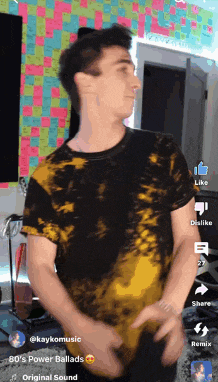 a man in a black and yellow tie dye shirt is dancing in front of a colorful wall