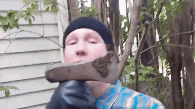 a man wearing a hat and gloves is holding a large piece of wood in his hand .