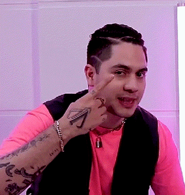 a man wearing a pink shirt and a black vest has a tattoo on his right hand