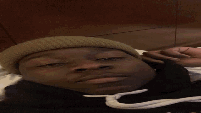 a man wearing a beanie and a black hoodie is laying down and giving the peace sign