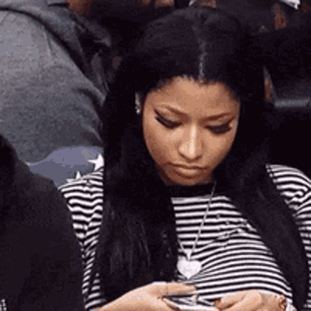 a woman in a striped shirt is looking at her cell phone .