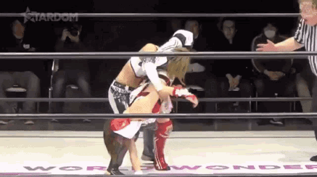 two women are wrestling in a ring while a referee looks on .