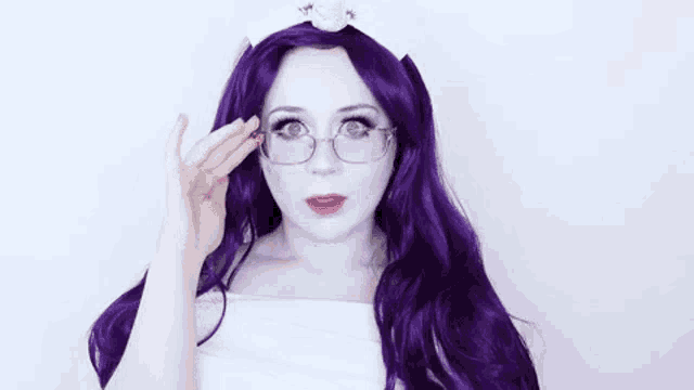 a woman with purple hair and glasses is wearing a white shirt and a white headband .