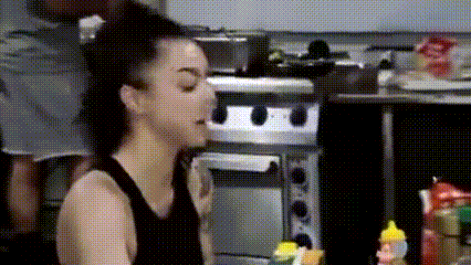 a woman is sitting at a table in a kitchen with a bottle of ketchup in front of her .