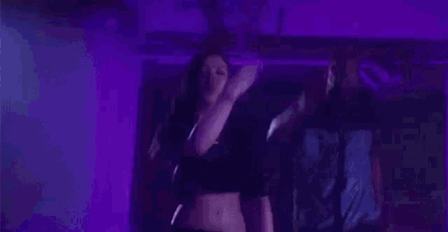 a woman in a crop top is dancing in a dark room with purple lights .