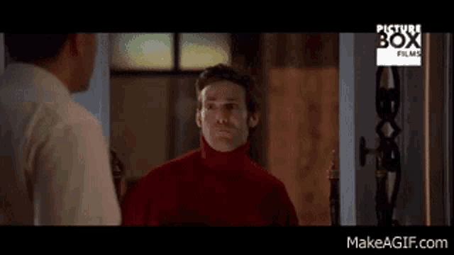 a man in a red turtleneck is talking to another man in a white shirt .