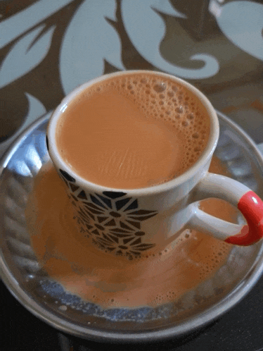 a cup of tea sits on a saucer with a red handle