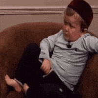 a little boy is sitting on a couch wearing a hat and a blue shirt .
