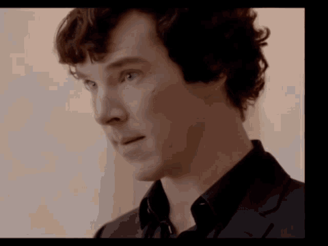 a man with curly hair wearing a black suit and black shirt