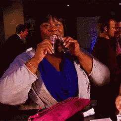 a woman in a blue shirt is drinking a glass of wine