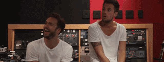 two men in white shirts are laughing in a room with a red and black wall
