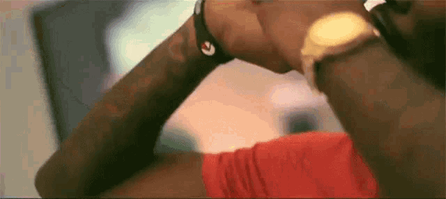a man wearing a red shirt and a gold watch is looking at his watch .