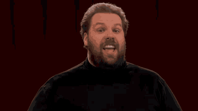a man with a beard is smiling and wearing a black turtleneck