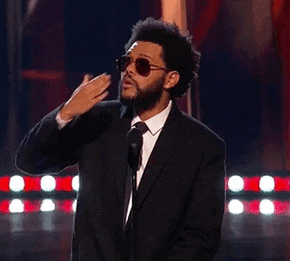 a man wearing sunglasses and a suit is standing in front of a microphone on a stage .