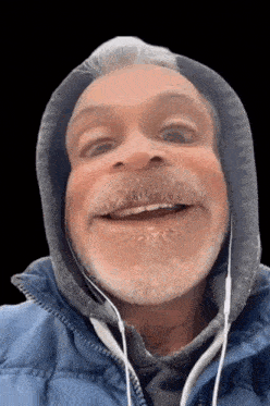 a man with a beard wearing a blue jacket and headphones makes a funny face