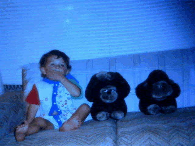 a little girl sitting on a couch with two stuffed gorillas behind her