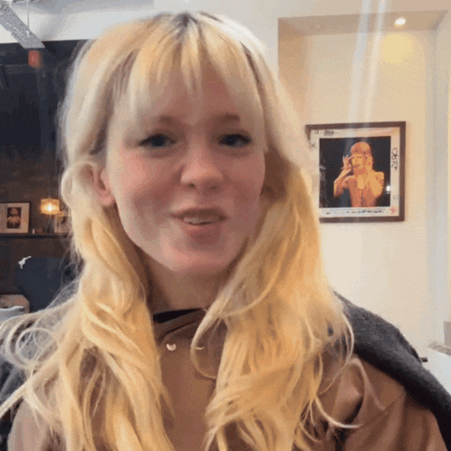 a woman with blonde hair is standing in front of a framed picture of taylor swift