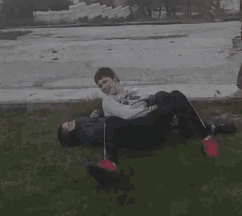 two boys are laying on the grass with one wearing a sweatshirt that says ' sd ' on it