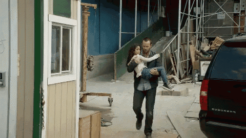a man is carrying a little girl in his arms in front of a suburban car