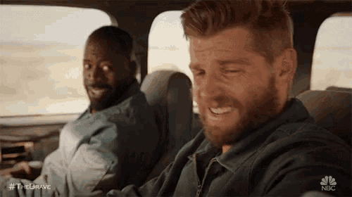 two men are sitting in the back seat of a car . one of the men is smiling and the other is crying .