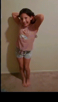a little girl in a pink shirt and shorts is standing with her hands behind her head