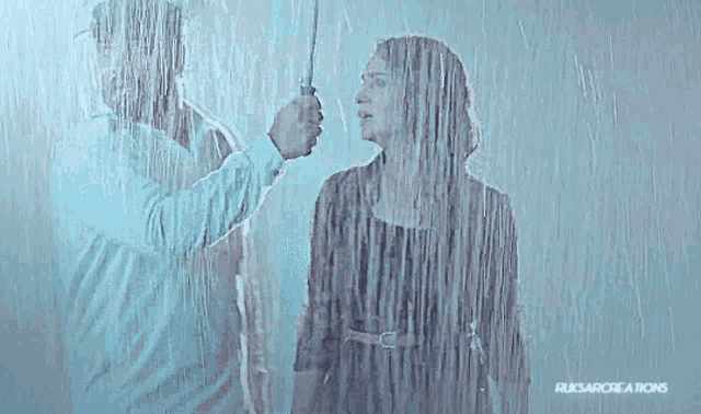 a man and a woman are standing in the rain behind a glass .