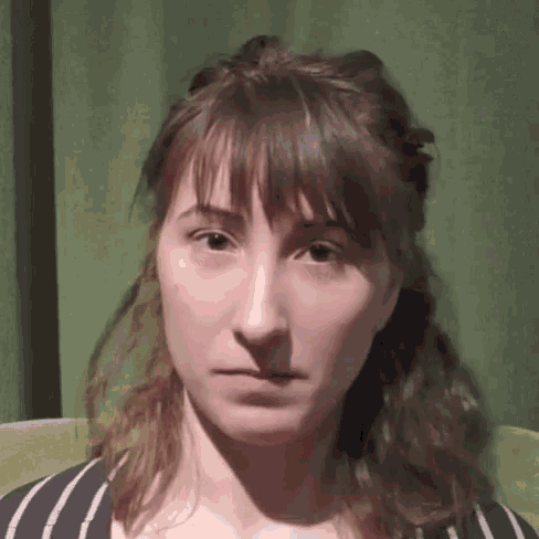 a close up of a woman 's face with a striped shirt and a green curtain behind her .