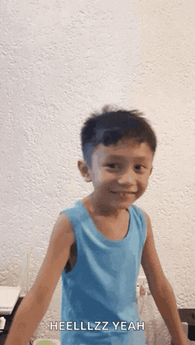 a young boy in a blue tank top is smiling and making a funny face .