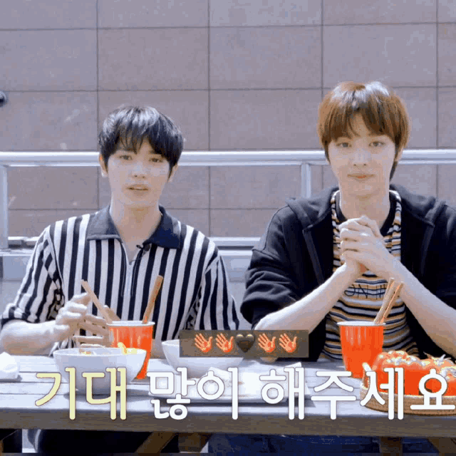 two young men are sitting at a table with a sign that says ' i love you '