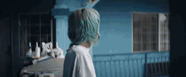 a woman with blue hair stands in front of a blue wall
