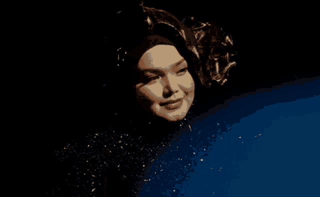 a woman wearing a black hijab is smiling in front of a dark background