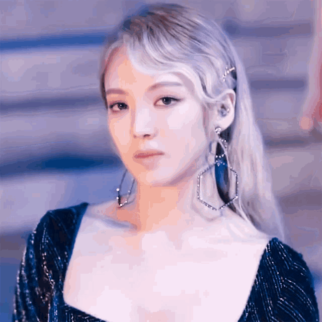 a woman with long blonde hair wearing a blue dress and earrings