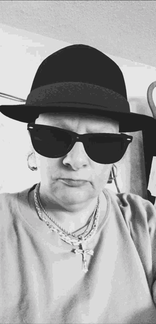 a woman wearing a hat and sunglasses has a cross on her neck