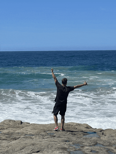 a man with his arms outstretched stands on a rocky cliff overlooking the ocean