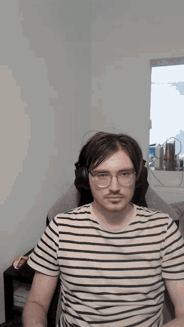 a man wearing glasses and a striped shirt sitting in a chair