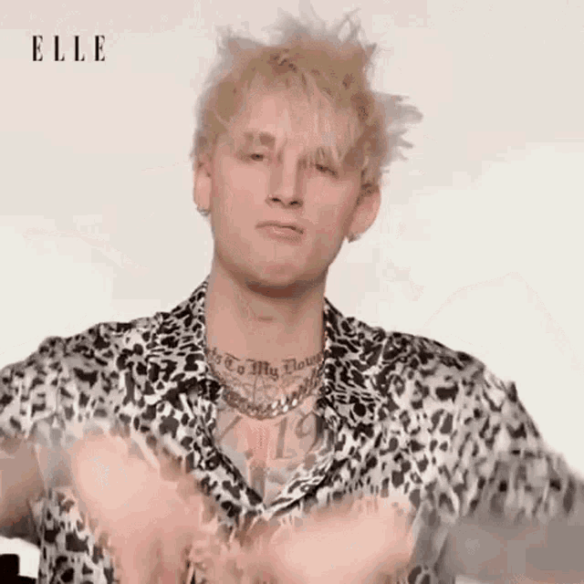 a man with a tattoo on his neck is wearing a leopard print shirt and making a funny face .
